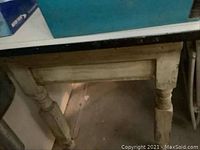 Close-up of table leg showing turned wooden design and distressed paint