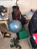 Wide shot of the golf bag, three clubs, exercise ball, green mats, and other fitness items on the floor.