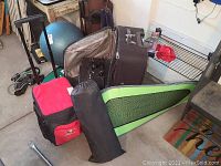 Overview photo showing three luggage bags and one folding chair in carrying bag on concrete floor in garage