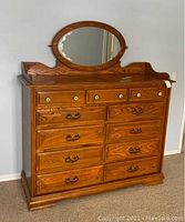Front view of chest showing 11 drawers and attached oval mirror with decorative etching.