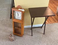 Three items arranged on carpet: pine wall clock, wooden TV table, and wooden bunny door stop.