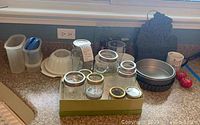 Photo showing 15 kitchen items on counter including glass jars, Tupperware containers, baking pans, ramekins, kitchen torch, and Michigan state wall art.