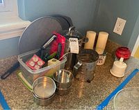 Various kitchen and baking items grouped on countertop including pans, thermometers, sifter, candles and utensils