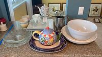 Photo of various serving bowls, teapot with rooster design, pitchers, and small glass bowls on a kitchen counter