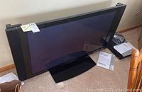 Front angle view of Elite Pioneer 43-inch plasma TV on stand with manuals and receiver unit on floor next to it.