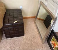 Faux leather storage trunk and beveled mirror next to wall on carpeted floor