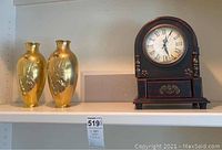 Brass floral vases display alongside the mantle clock on shelf.