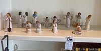 Full view of 12 Willow Tree angel figurines arranged on shelves showing various poses and angelics with wire wings.
