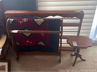 Photo showing custom wooden China wall display rack, wooden quilt rack with quilt, and small side table positioned near window.