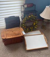 Full lot group showing picnic basket, black metal magazine rack, metal wall rack, wreath, breakfast trays, and partial side table with lamp