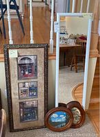 Wide photo showing all four items grouped near stairs: a tall white framed mirror, large ornate framed vertical French storefront print, and two small oval framed paintings with outdoor scenes.