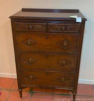 Front view of antique wooden chest with four drawers shows carved details and metal ring pulls.