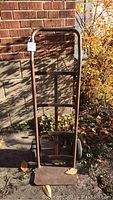 Full view of the metal furniture dolly leaning against a brick wall showing the entire frame and base plate.