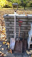 Three short handle shovels lined up against a brick wall outdoors, showing different blade materials and handle conditions.