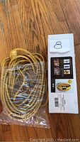 Yellow extension cord coiled and wrapped in plastic on wooden floor with packaging box nearby.