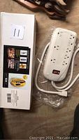 White Leviton power bar with attached white power cord and power switch, shown beside original box.