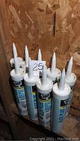 Lot of nine tubes of DAP Alex Plus acrylic latex caulk plus silicone, white, for windows and doors, standing upright with nozzles visible.