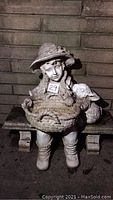 Full view of the girl statue seated with basket and bunny on stone bench.