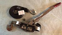 Manual come-along wench with red handle and black strap with hook laid on floor