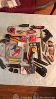 Full lot spread on flat surface showing a variety of hand tools including tape measures, pliers, Allen keys, knives, and a staple gun.