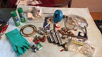 Assorted plumbing parts spread out on table including faucet, valves, gloves, toilet snake, tape
