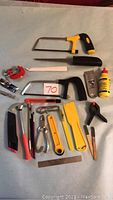 Photo showing a variety of hand tools laid out on a white sheet including saws, hammer, paintbrushes, clamps, glue bottle, and scrapers.