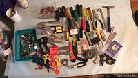 Photo showing varied hand tools including screwdrivers, pliers, clamps, cutting tools, hammer, measuring tape, and level arranged on a surface.