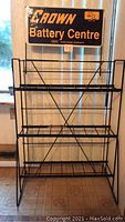 Full front view of the black metal collapsible display stand with three shelves and a Crown Battery Centre sign at the top.