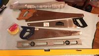 Three hand saws, two spirit levels and a roll of insect screening on table