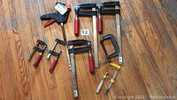 Full lot of 8 vices and clamps arranged on wooden floor.