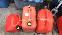 Photo of three red gas containers placed side by side on the ground, showing size variations and condition.