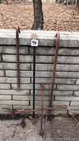 Five crowbars and one tire iron shown leaning against a low brick wall with dried leaves on the ground.