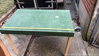 Full view of one wooden work table with green top and natural wood legs placed outdoors