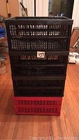 Stacked view of four collapsible plastic storage bins, three black and one red, showing their size and folding structure.
