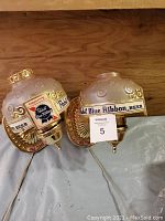 Two Pabst Blue Ribbon beer-themed wall lamps placed side by side, showing the front view with branded logos and gold accents.