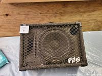 Front view of PAS PA speaker cabinet with metal mesh grille and speaker cone visible.