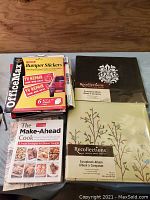 Stack of books including OfficeMax bumper stickers, The Make-Ahead Cook, and two Recollections scrapbooks on top