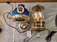 Two vintage branded wall light fixtures side by side, Pabst Blue Ribbon and Michelob, showing overall condition and discoloration on PBR shade