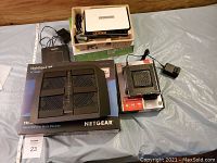 Overview of all devices including routers, modems, cables, and power adapters displayed on table including boxed Netgear Nighthawk X6 router and assorted devices.