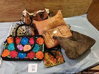 Multiple purses and a wallet arranged on a flat surface showing color and size variation, including a tan leather purse, brown suede purse, floral embroidered purse and others.