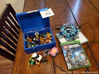 Xbox One Lego Dimensions game case, game disc, Lego Dimensions portal toy with cable, assorted Lego figures and accessories in and around a blue box on wooden table.