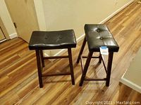 Pair of bar stools placed on wood flooring showing leather cushion tops and wooden legs from an angle
