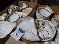 Boxes containing Mikasa Everest pattern china plates, bowls, cups, and saucers stored in white quilted zippered protective bags.