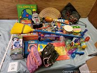 Photo showing entire lot on table including mitts, musical toys, bobblehead, costume accessories, and science kit.