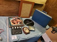Photo of all lot items including blue briefcase, vinyl records, director's slate, wooden picture frame without glass, small wall decor dog picture, CDs, and Audio-Technica slip mat.