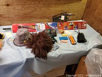 Table with various outdoor sports items such as ski/snowboard wax, a kite box, knee pads, hat, pedometers, bike cargo rack, and blue and orange table tennis net