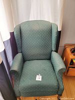 Green wingback chair with subtle dotted fabric upholstery, showing visible wear especially on the armrests and seat cushions.