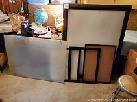 Five items laid out: one oversized black frame, three medium black frames, one with glass, and a large frosted or heavy glass sheet lying on the floor.