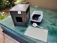 Side views of the entire cat litter box set on an outdoor surface showing all included components: litter box enclosure, plastic tray, scooper, and paw mat.