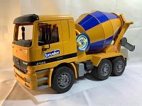 Front angled view of yellow and blue Bruder Mercedes cement mixer toy truck showing front grille with Mercedes logo, six wheels, and mixing drum with control dial.